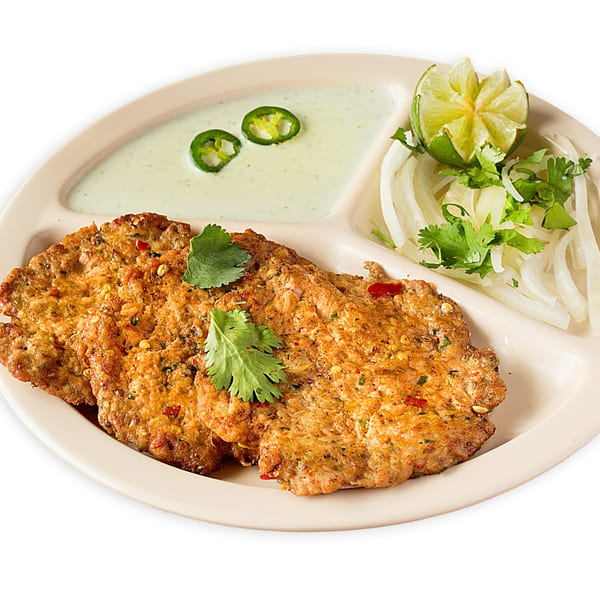 Three golden-brown Pakistani chapli kebabs with cilantro, a side of green sauce, and onion salad.
