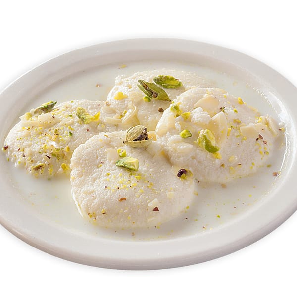 Four Ras Malai pieces, a Pakistani dessert, garnished with pistachios and cardamom pods in milk.