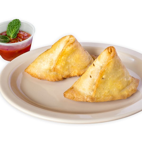 Two golden-brown samosas with cumin seeds on a plate, served with a side of red chutney and mint.