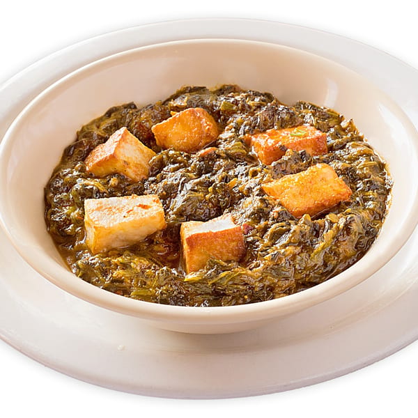 A bowl of Asma's Cuisine's Pakistani saag paneer, a green spinach dish with golden fried cheese cubes.