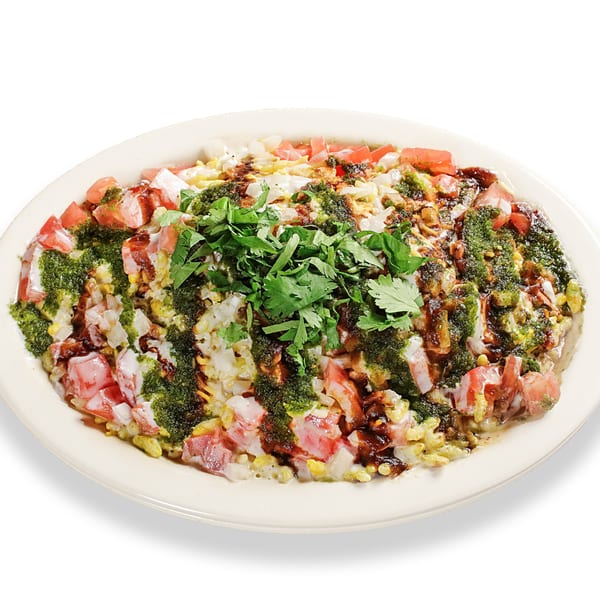 A vibrant Pakistani chaat dish, topped with fresh cilantro, green chutney, and diced tomatoes.