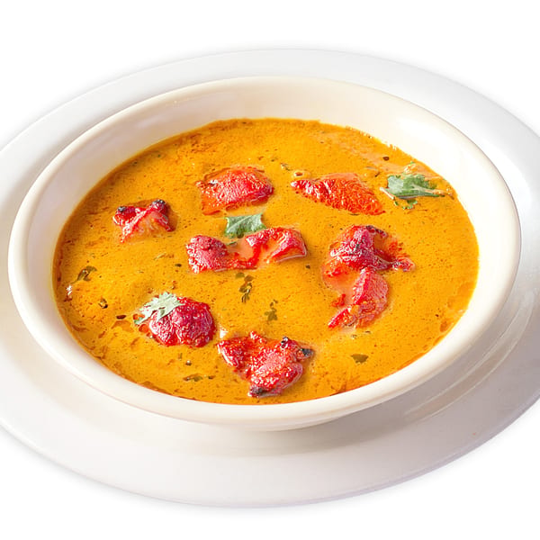 A bowl of Asma's Cuisine chicken tikka masala, featuring red chicken pieces in a rich orange sauce.