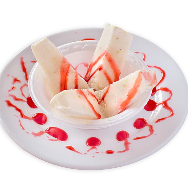 Pakistani Kulfi, a frozen dessert, drizzled with red syrup, served in a white bowl on a plate.