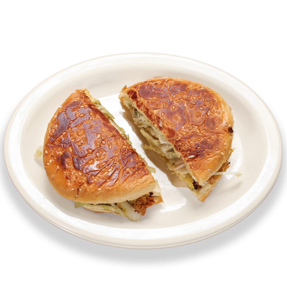 Two halves of a Pakistani bun kebab, filled with meat and onions, on a white plate.