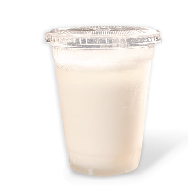 A clear plastic cup filled with a cold, light-colored beverage, possibly a Pakistani lassi.