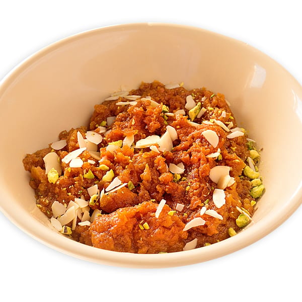 A bowl of orange Pakistani halwa, garnished with slivered almonds and chopped pistachios.