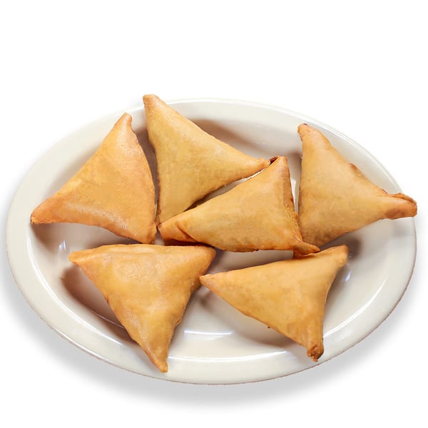 A white oval plate holds six golden-brown, triangular Pakistani samosas, fried to perfection.